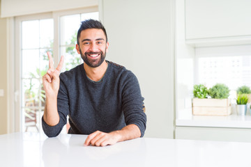 Handsome hispanic man wearing casual sweater at home showing and pointing up with fingers number two while smiling confident and happy.