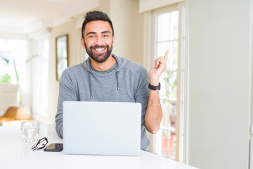 Handsome hispanic man working using computer laptop very happy pointing with hand and finger to the side