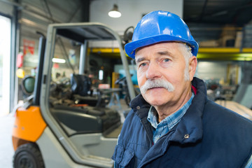 portrait of senior man in front of forklift truck