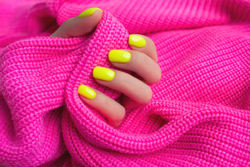 Stylish trendy female manicure. Neon yellow nails on plastic pink background. Nail polish. Art manicure. Modern style.