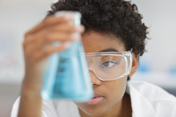 woman in glasses looks at the blue liquid in flask