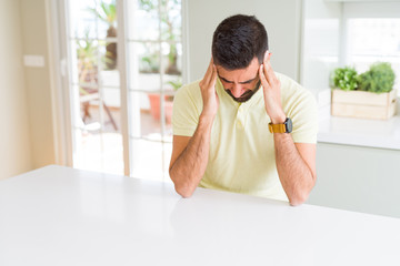 Handsome hispanic man casual yellow t-shirt at home suffering from headache desperate and stressed because pain and migraine. Hands on head.