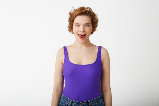 Photo of happy funny young cute short-haired girl, looking at the camera and licking, presenting a delicious dessert, stands over white background.