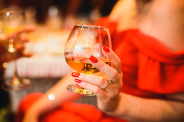 A glass of brandy in the hands of a girl in a red dress