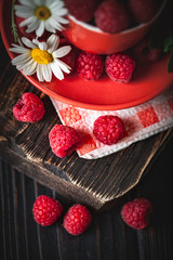 Raspberry in a red cup with chamomile and leaves on a dark background. Summer and healthy food concept. Selective focus.