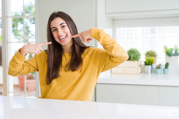 Beautiful young woman wearing yellow sweater smiling confident showing and pointing with fingers teeth and mouth. Health concept.