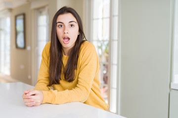 Beautiful young woman wearing yellow sweater afraid and shocked with surprise expression, fear and excited face.