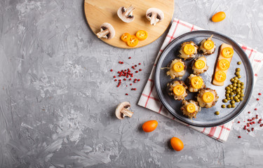 stuffed fried champignons with cheese, kumquats and green peas on a gray concrete background. top view, copy space.