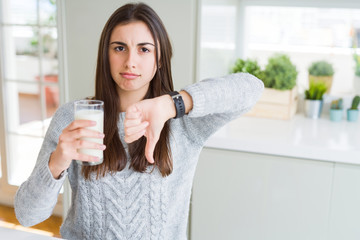 Beautiful young woman drinking a glass of fresh milk with angry face, negative sign showing dislike...