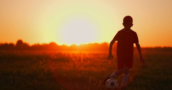 A boy with a football runs to the camera at sunset
