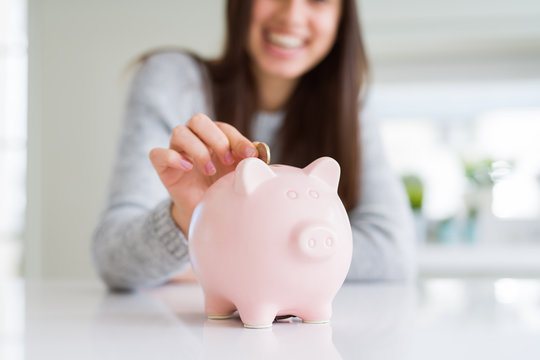 Young woman smiling putting a coin inside piggy bank as savings for investment