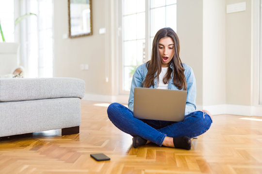 Beautiful young woman sitting on the floor with crossed legs using laptop scared in shock with a surprise face, afraid and excited with fear expression