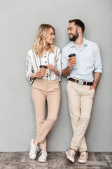 Full length photo of european couple in casual clothing holding paper cups and looking at each other