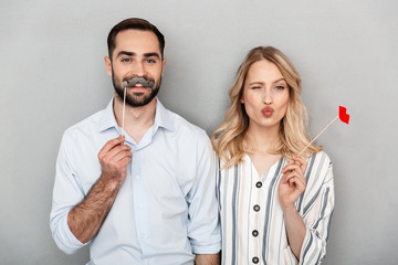 Photo closeup of joyful couple in casual clothing having fun with paper fake mustaches and lips on stick