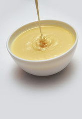 Pouring condensed milk with sugar in a bowl isolated on gray