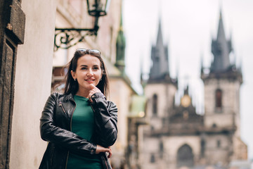 Fototapeta premium Street portrait of adorable brunette woman with long hair posing at Old Town Square in Prague. smiling pretty brunette girl, lifestyle. observatory of astronomical clock tower in Prague, Czech