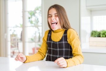 Young beautiful blonde kid girl wearing casual yellow sweater at home sticking tongue out happy with funny expression. Emotion concept. © Krakenimages.com