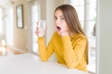 Beautiful young girl kid drinking a fresh glass of water scared in shock with a surprise face, afraid and excited with fear expression
