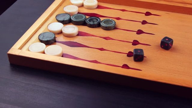 Backgammon game. Human rolls the dice on the backgammon board against the background of checkers. Close-up