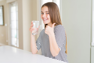 Beautiful young girl kid drinking a fresh glass of water happy with big smile doing ok sign, thumb up with fingers, excellent sign