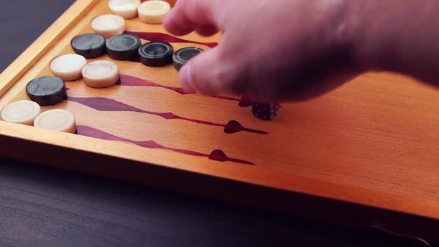 Backgammon game. Human rolls the dice on the backgammon board against the background of checkers. Close-up
