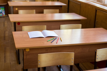 clean notebook and colored pencils on the desk in empty classroom. Concept of school education.