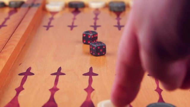 Backgammon game. Human rolls the dice on the backgammon board against the background of checkers. Close-up
