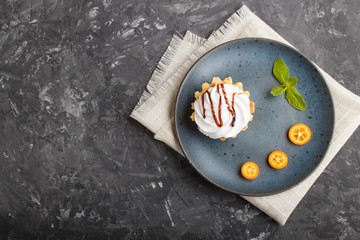 Cake with whipped egg cream on a blue ceramic plate with kumquat slices and mint leaves on a black concrete background. top view, copy space.