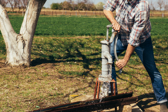 man pumping water from draw well on farm