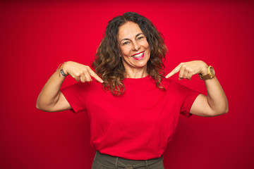 Middle age senior woman with curly hair over red isolated background looking confident with smile...
