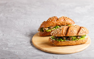 Sprats sandwiches with lettuce and cream cheese on wooden board on a gray concrete background.