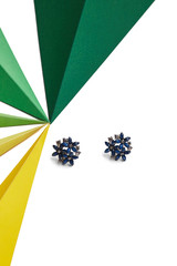 Shot of massive earrings, adorned with navy blue crystals which form flowers together. The accessory is isolated on snowy background near multicolored blue 3-dimensional triangles of different size.