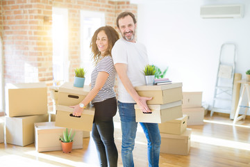 Middle age senior couple moving to a new house, holding cardboard boxing smiling happy in love with apartmant