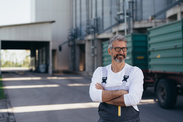worker standing crossed arms, blurred grain silo in background