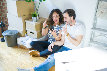 Middle age senior couple moving to a new home using smartphone surprised with an idea or question pointing finger with happy face, number one