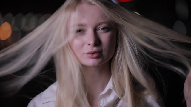 Sexy blonde woman posing touching her long hair in the night city, slow motion