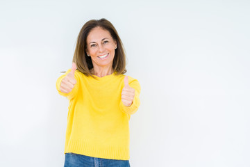 Beautiful middle age woman wearing yellow sweater over isolated background approving doing positive gesture with hand, thumbs up smiling and happy for success. Looking at the camera, winner gesture.