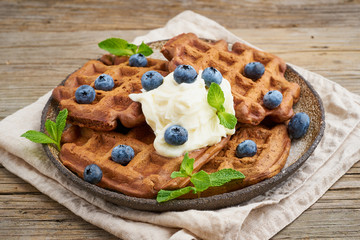 Chocolate banana waffles with blueberries, on dark wooden old table. Side view