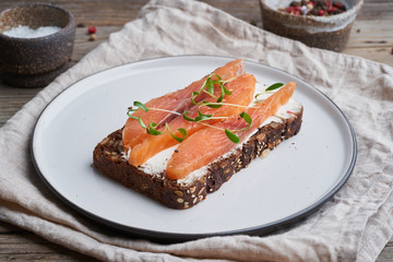 Rye bread with smoked salmon, cream cheese on old wooden table. Smorrebrod, the open danish sandwiches, side view.