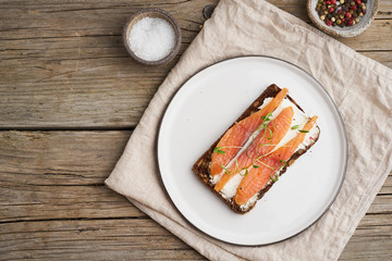Fototapeta na wymiar Smorrebrod, open danish sandwiches. Black rye bread with salmon, a cream cheese on old wooden table, top view, copy space