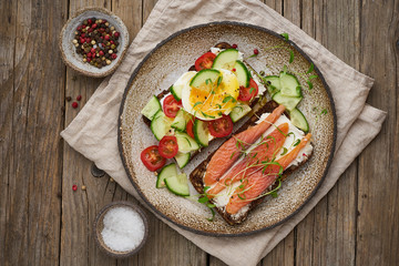 Smorrebrod - traditional Danish sandwiches. Black rye bread with salmon, cream cheese, cucumber, tomatoes on wooden table, top view.