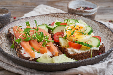 Smorrebrod - traditional Danish sandwiches. Black rye bread with a salmon, cream cheese, cucumber, tomatoes on wooden table, side view, close up