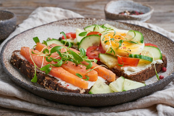 Smorrebrod - traditional Danish sandwiches. Black rye bread with a salmon, cream cheese, cucumber, tomatoes on wooden table, side view.