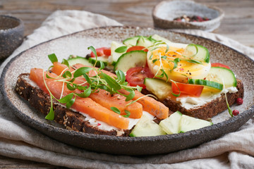 Smorrebrod - traditional Danish sandwiches. Black rye bread with a salmon, cream cheese, cucumber, tomatoes on wooden table, side view.