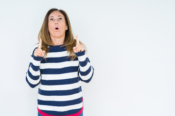 Beautiful middle age woman wearing navy sweater over isolated background amazed and surprised looking up and pointing with fingers and raised arms.