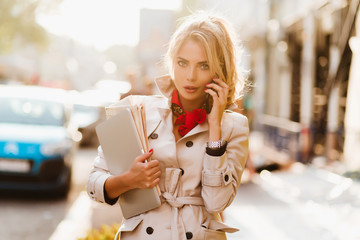 Tired business-lady carrying laptop and fresh newspapers to office in sunny morning. Outdoor...