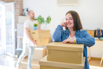 Young couple moving to new apartment, beautiful woman leaning on cardboard boxes and smiling happy