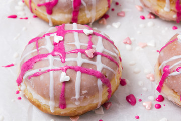 Traditional Polish donuts with pink frosting and heart sprinkles on light background. Tasty doughnuts with jam.