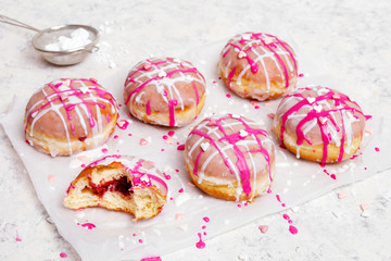 Traditional Polish donuts with pink frosting and heart sprinkles on light background. Tasty doughnuts with jam.
