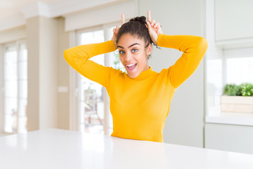Beautiful african american woman with afro hair wearing a casual yellow sweater Posing funny and crazy with fingers on head as bunny ears, smiling cheerful
